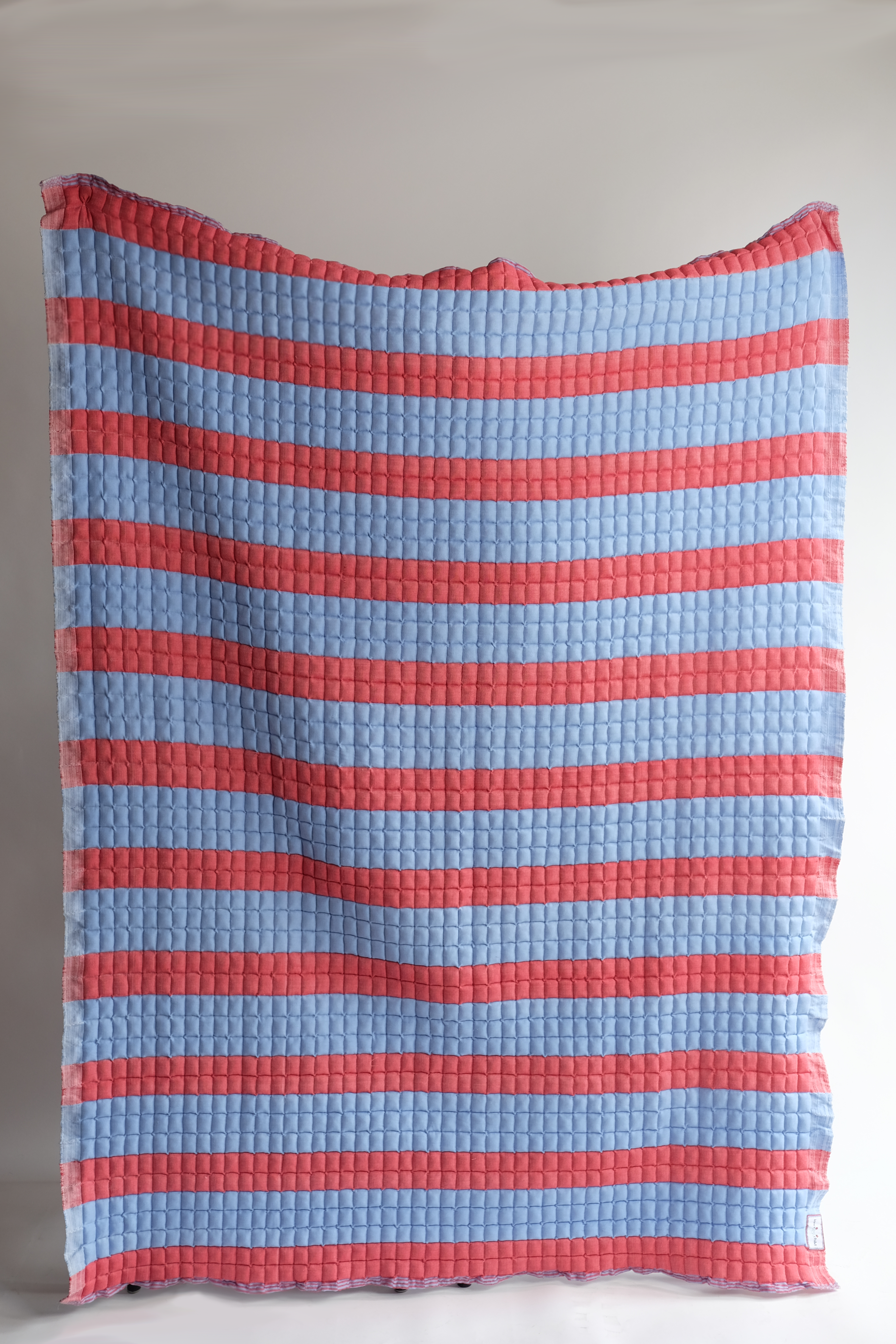 Red and blue striped sujani quilt hanging vertically
