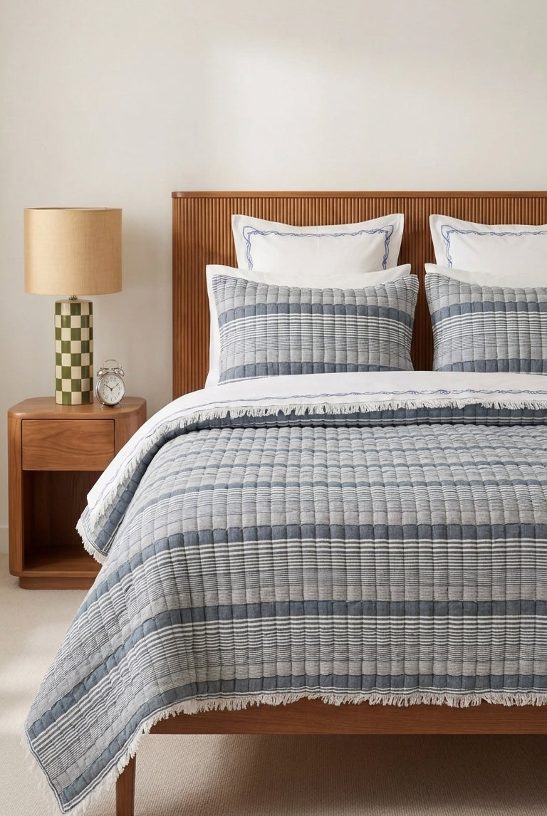 Bedroom with wooden bed, checkered blue and white duvet, and lamp on nightstand.