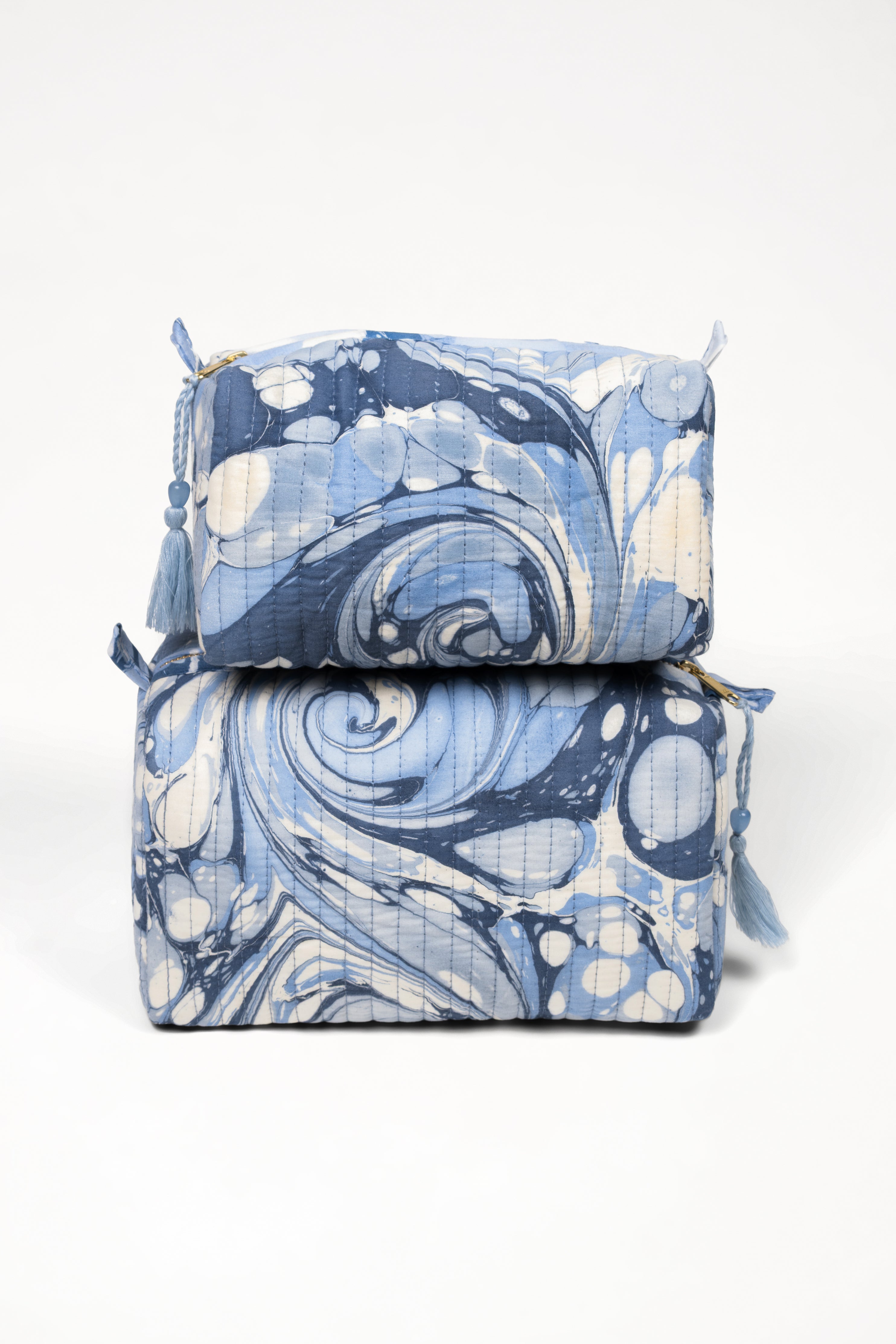 Stacked hand-marbled ocean wave cosmetic bags in blue and white swirl patterns