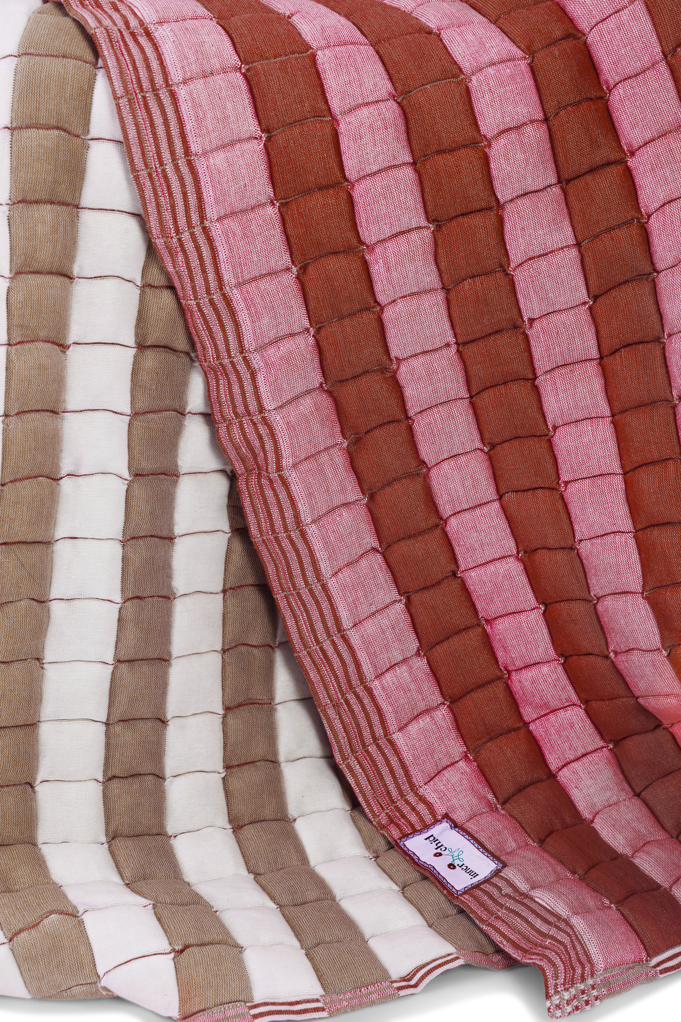 Close-up of warm taupe and beige reversible sujani quilts showcasing quilted texture