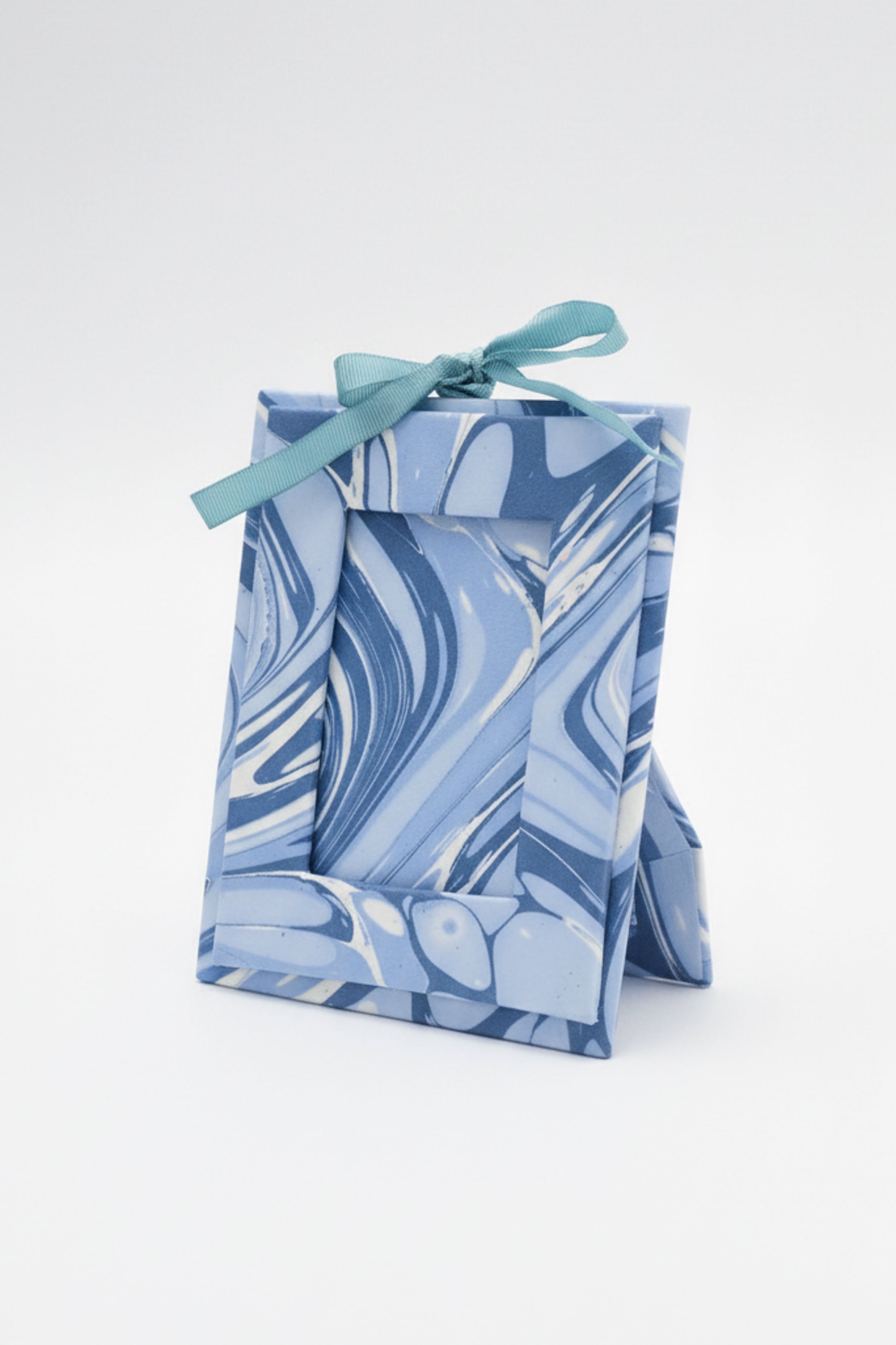 Mini hand-marbled ocean wave picture frame ornament standing upright with teal ribbon