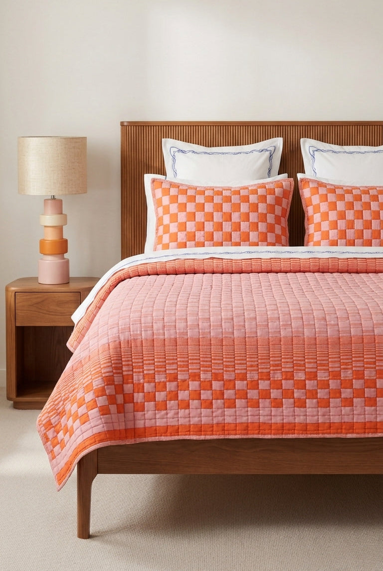 Bed with orange checkered quilt and wooden headboard in a room with a lamp.