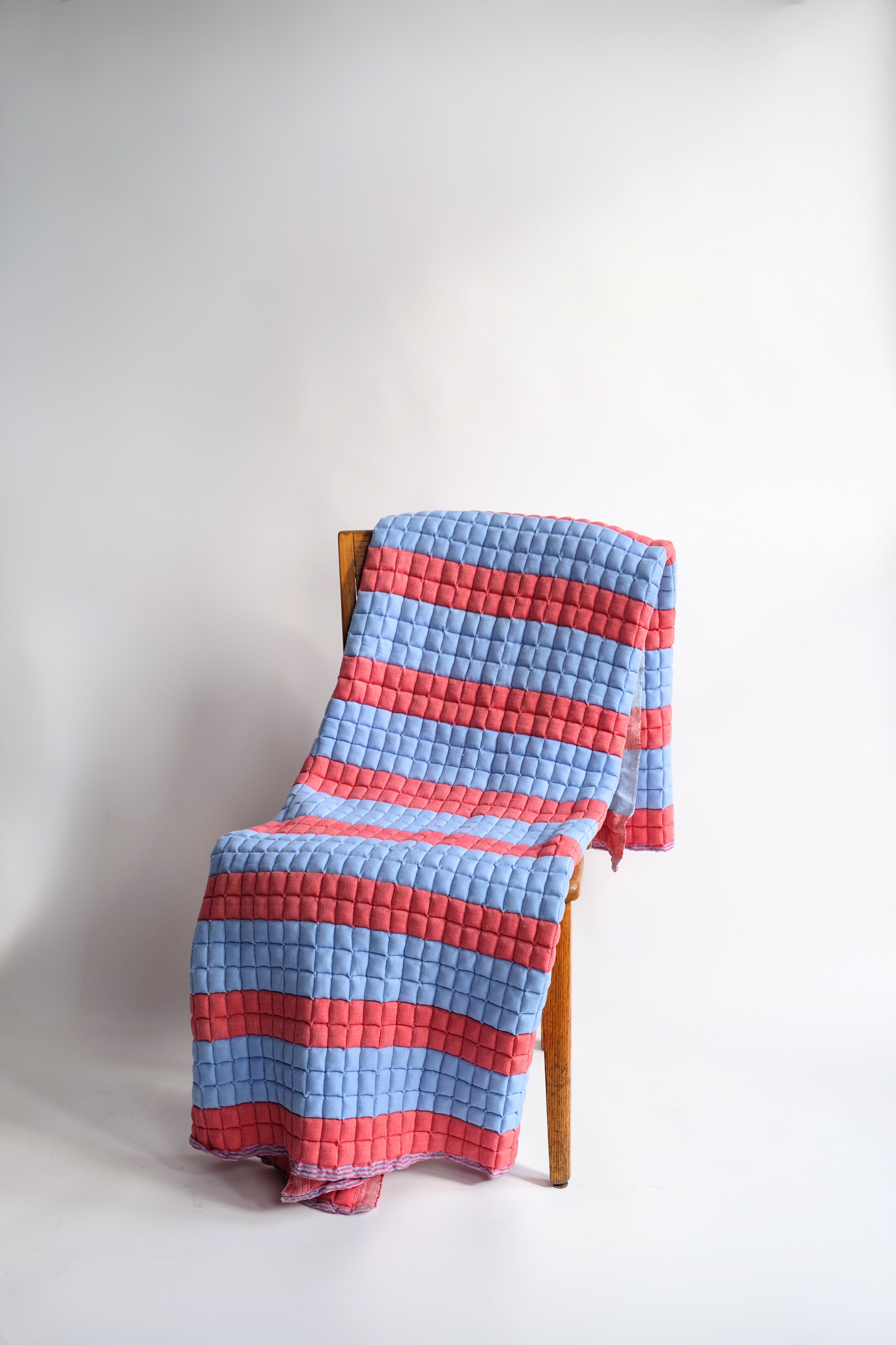 Red and blue striped sujani quilt draped over wooden chair