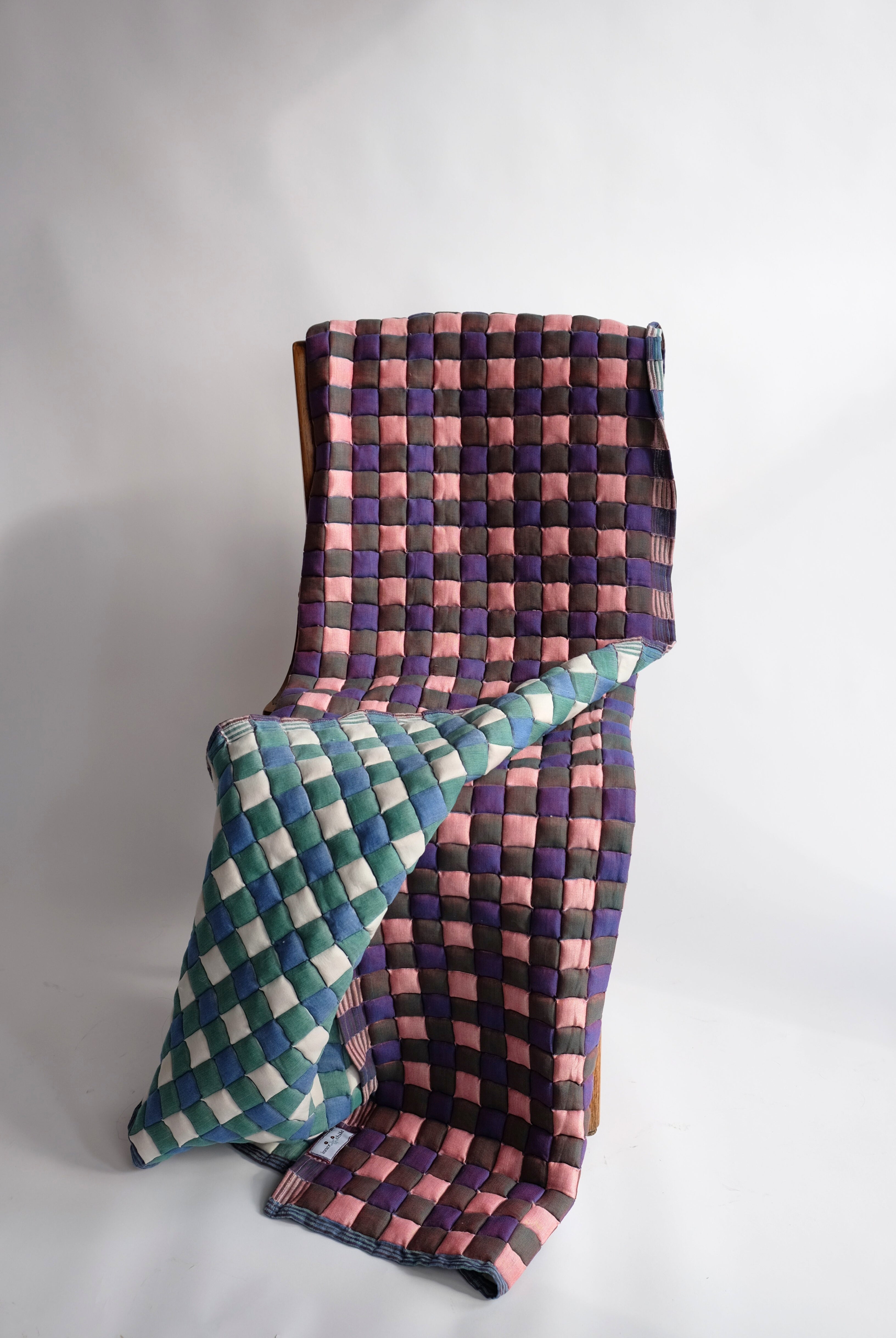 Purple and pink checkered reversible Sujani quilt with green-blue counterpart draped over chair