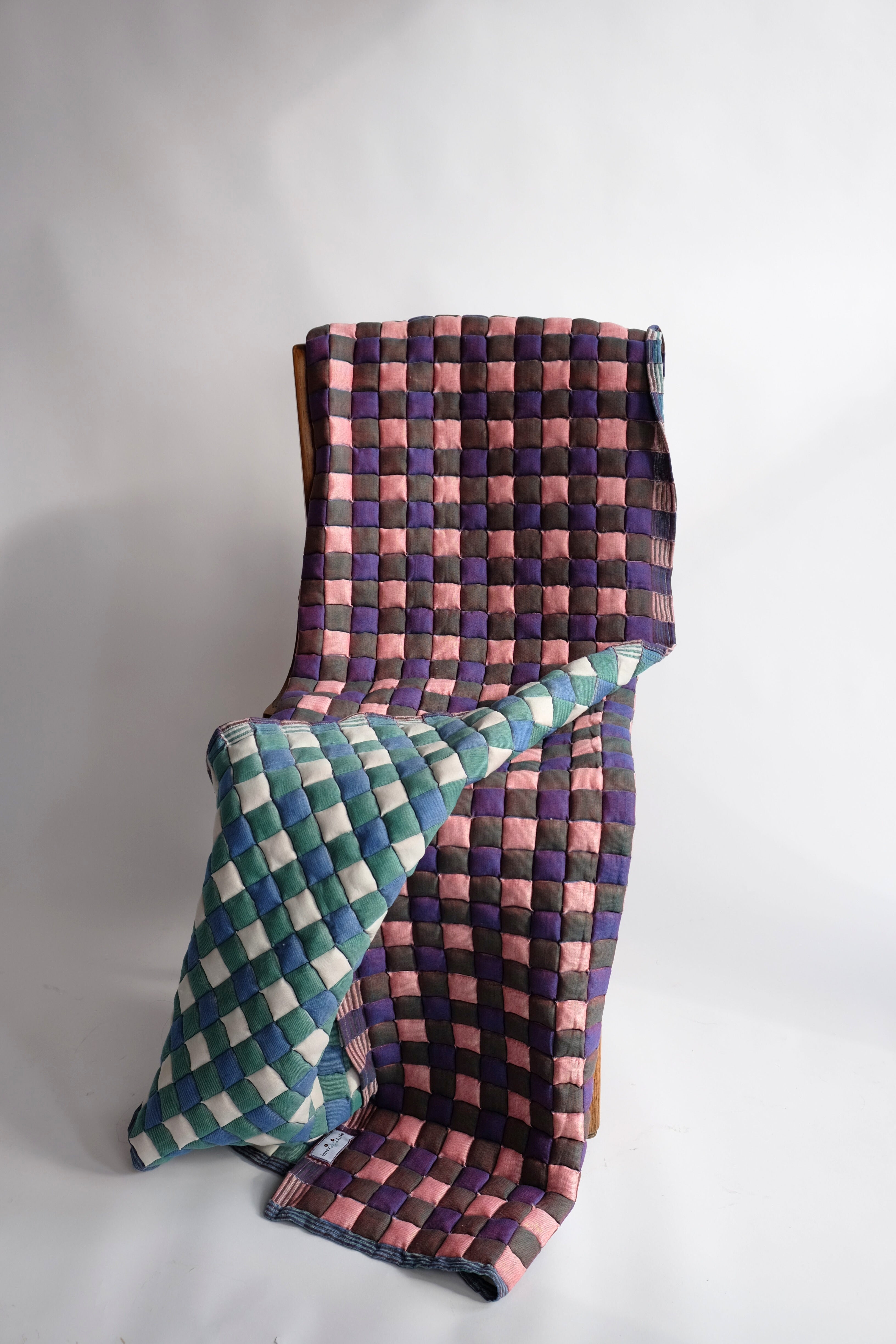 Purple and pink checkered reversible Sujani quilt with green-blue counterpart draped over chair