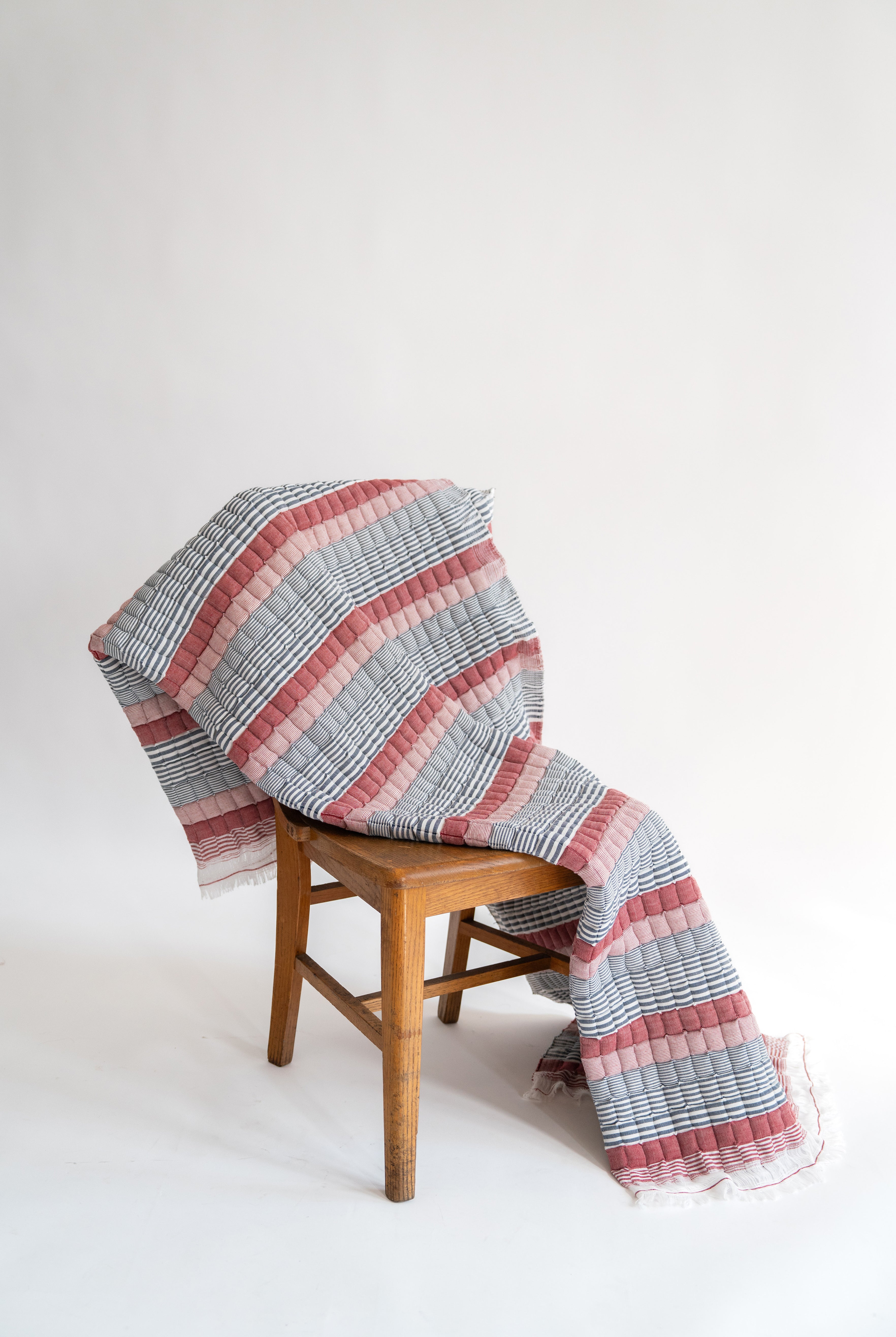 Inner Child's Americana Sujani quilt with red/pink and blue stripes draped over wooden chair