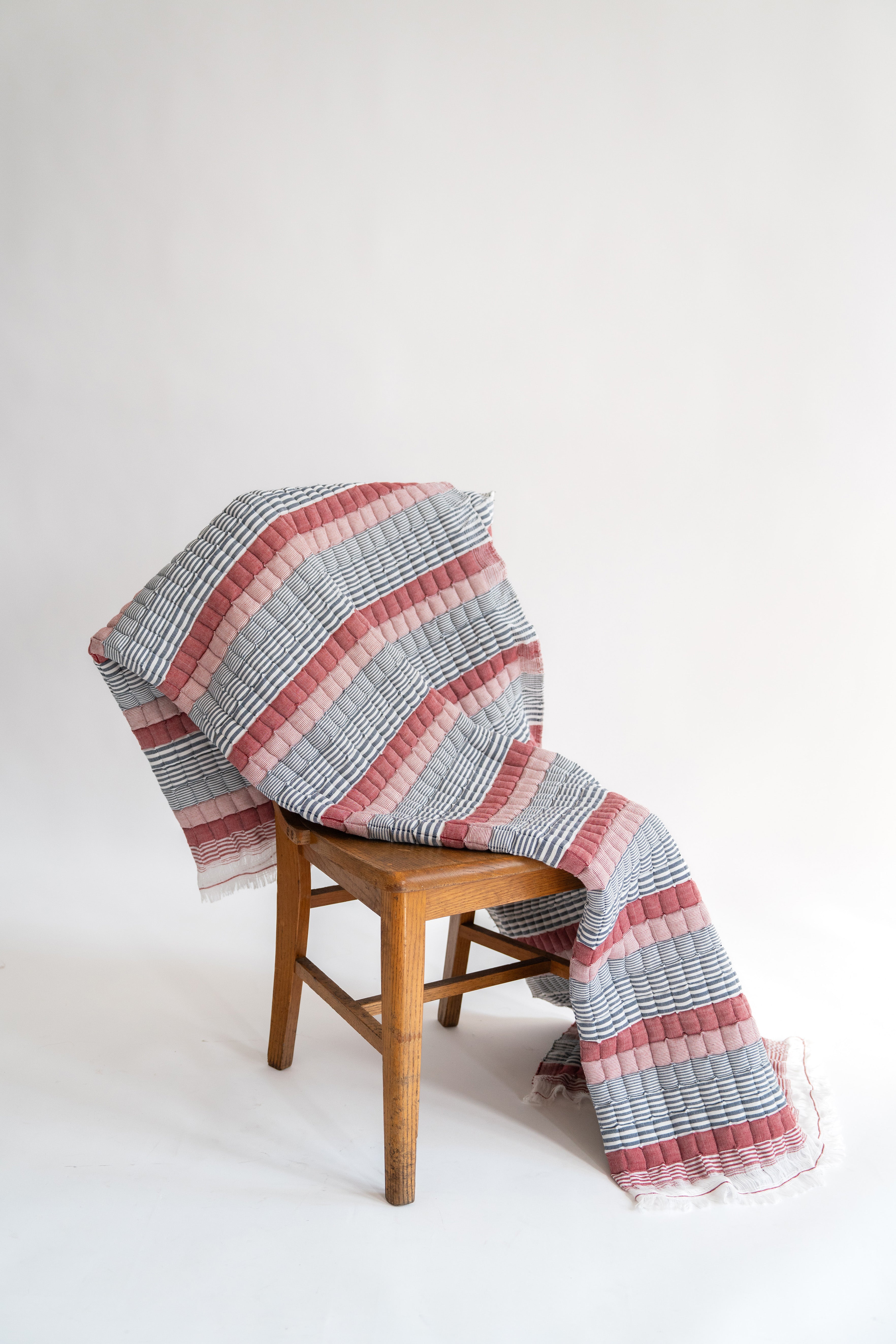 Inner Child's Americana Sujani quilt with red/pink and blue stripes draped over wooden chair