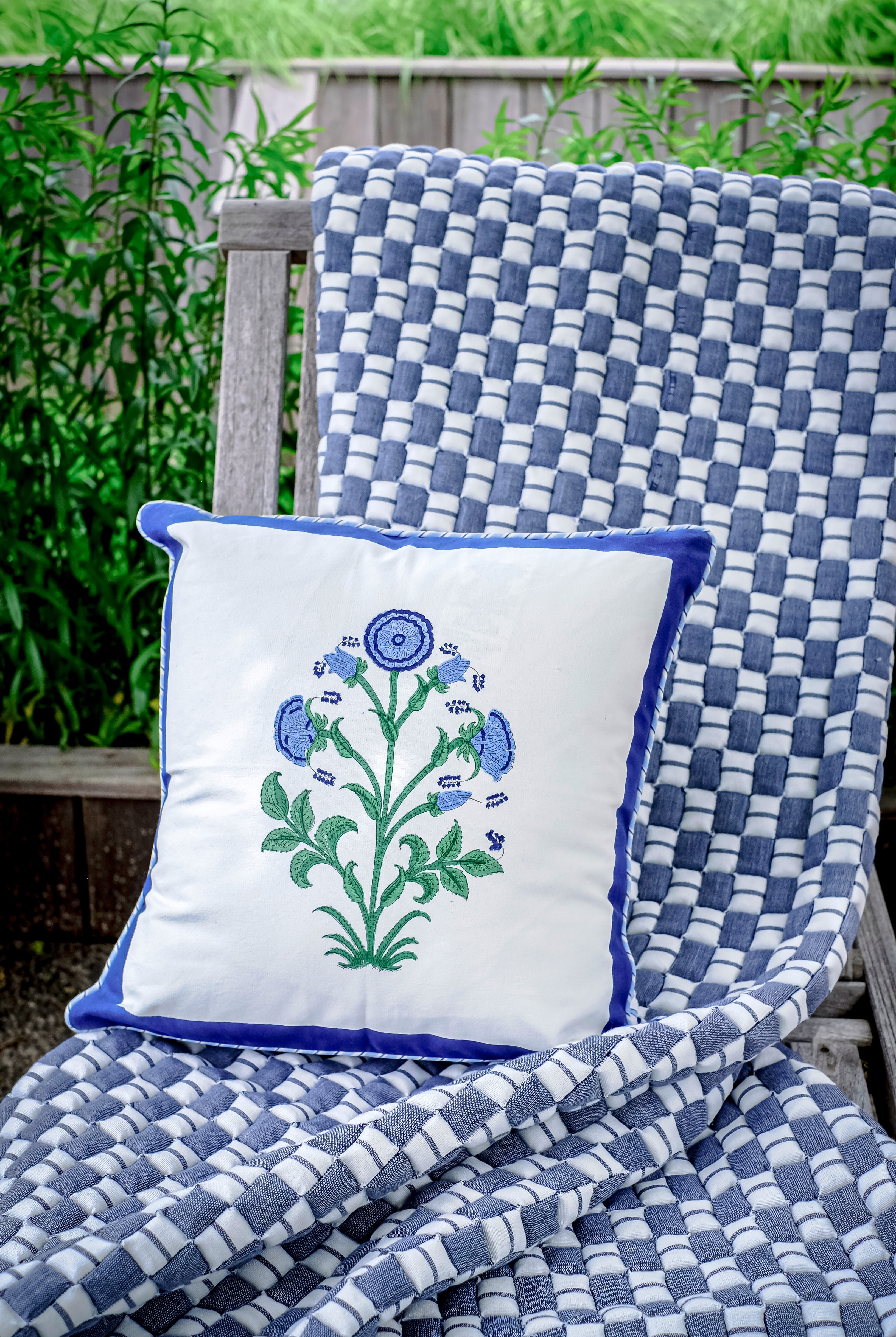 Blue checkered Sujani quilt with floral pillow on outdoor chair