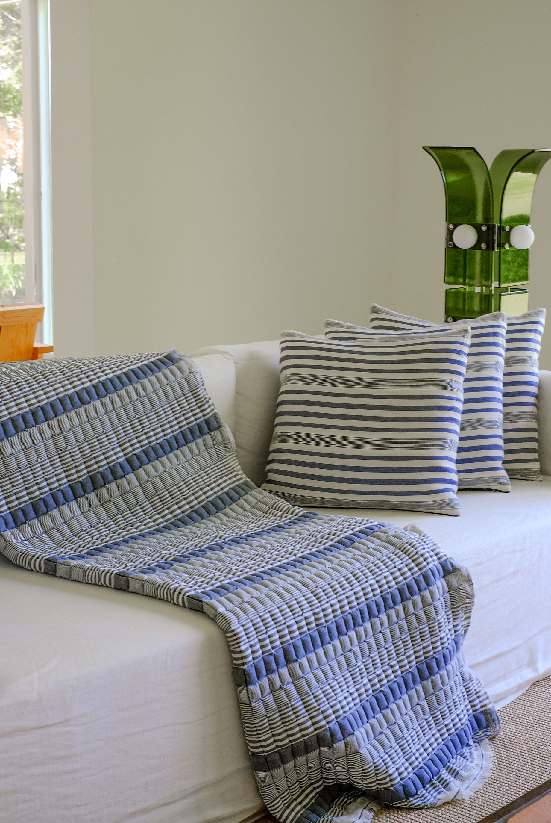 Blue striped Sujani quilt draped on white couch with matching pillows