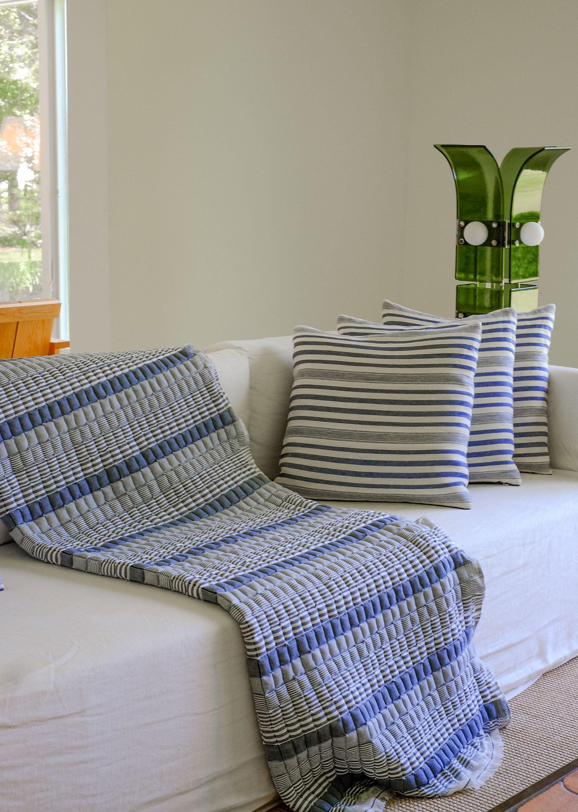 Blue striped Sujani quilt draped on white couch with matching pillows