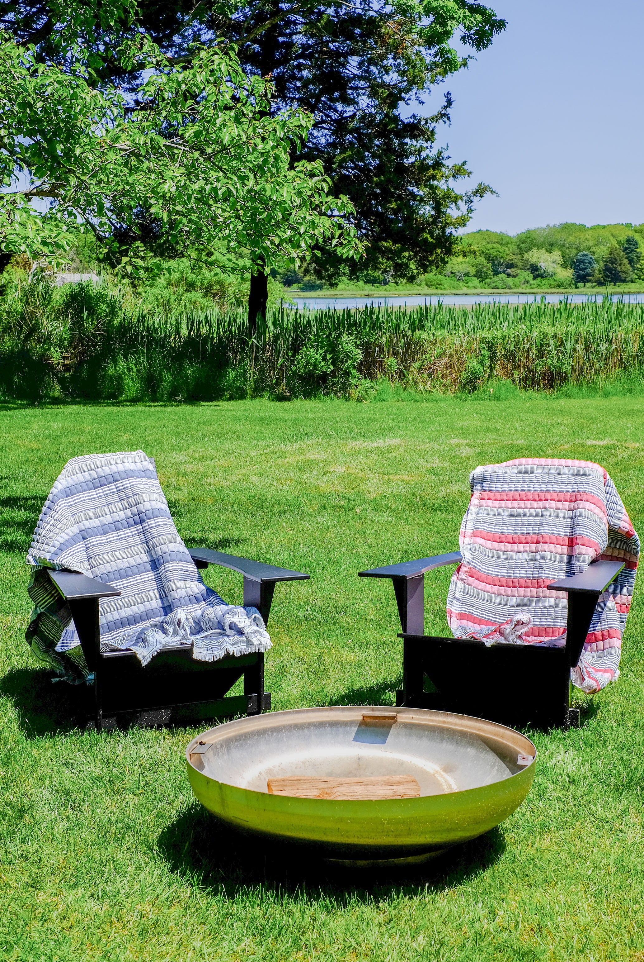 Inner Child Americana Sujani quilt with blue stripes draped over black chair near fire pit in sunny garden