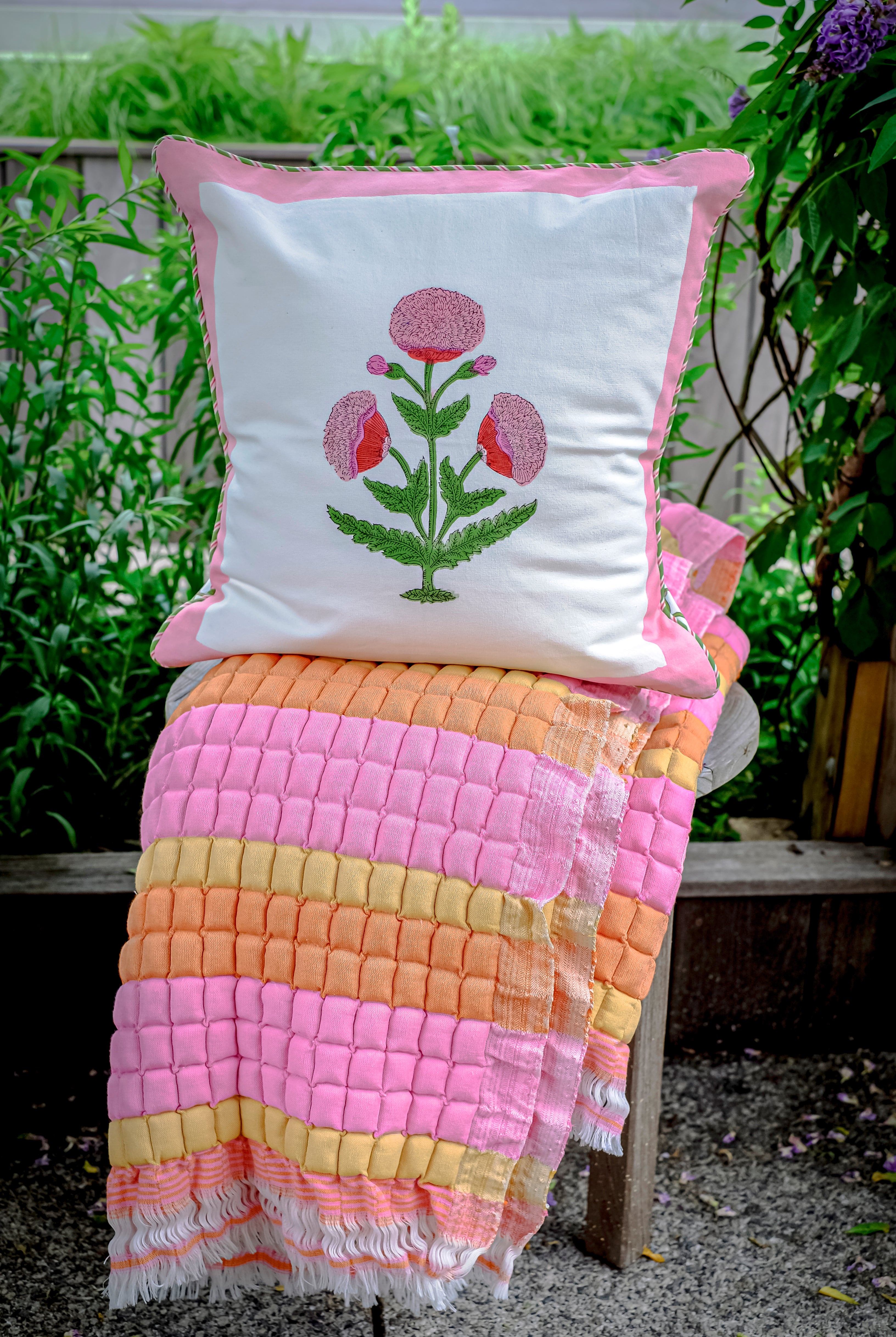 Inner Child Creamsicle Sujani quilt with floral pillow on outdoor bench