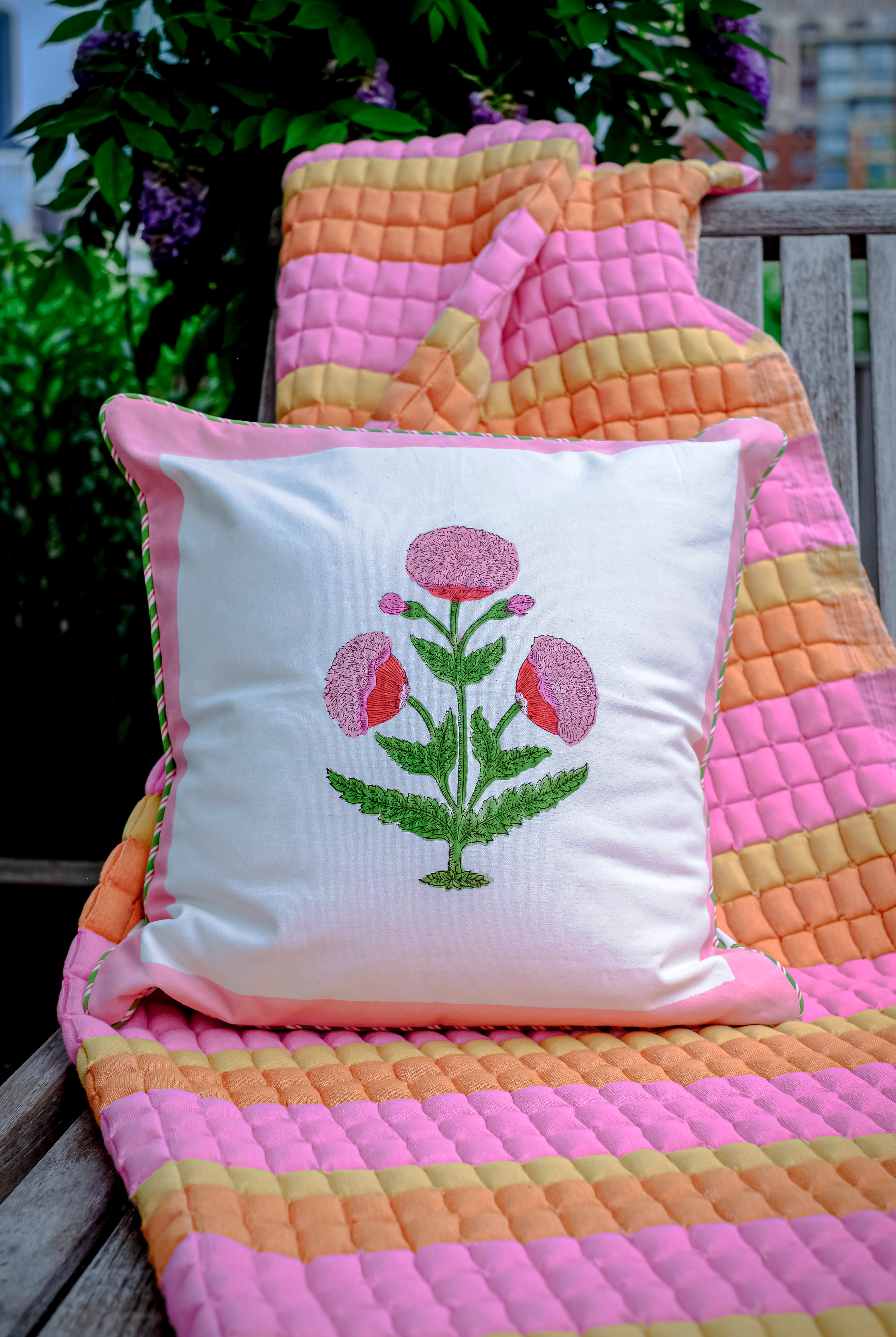 Inner Child Creamsicle Sujani quilt with floral pillow on wooden bench