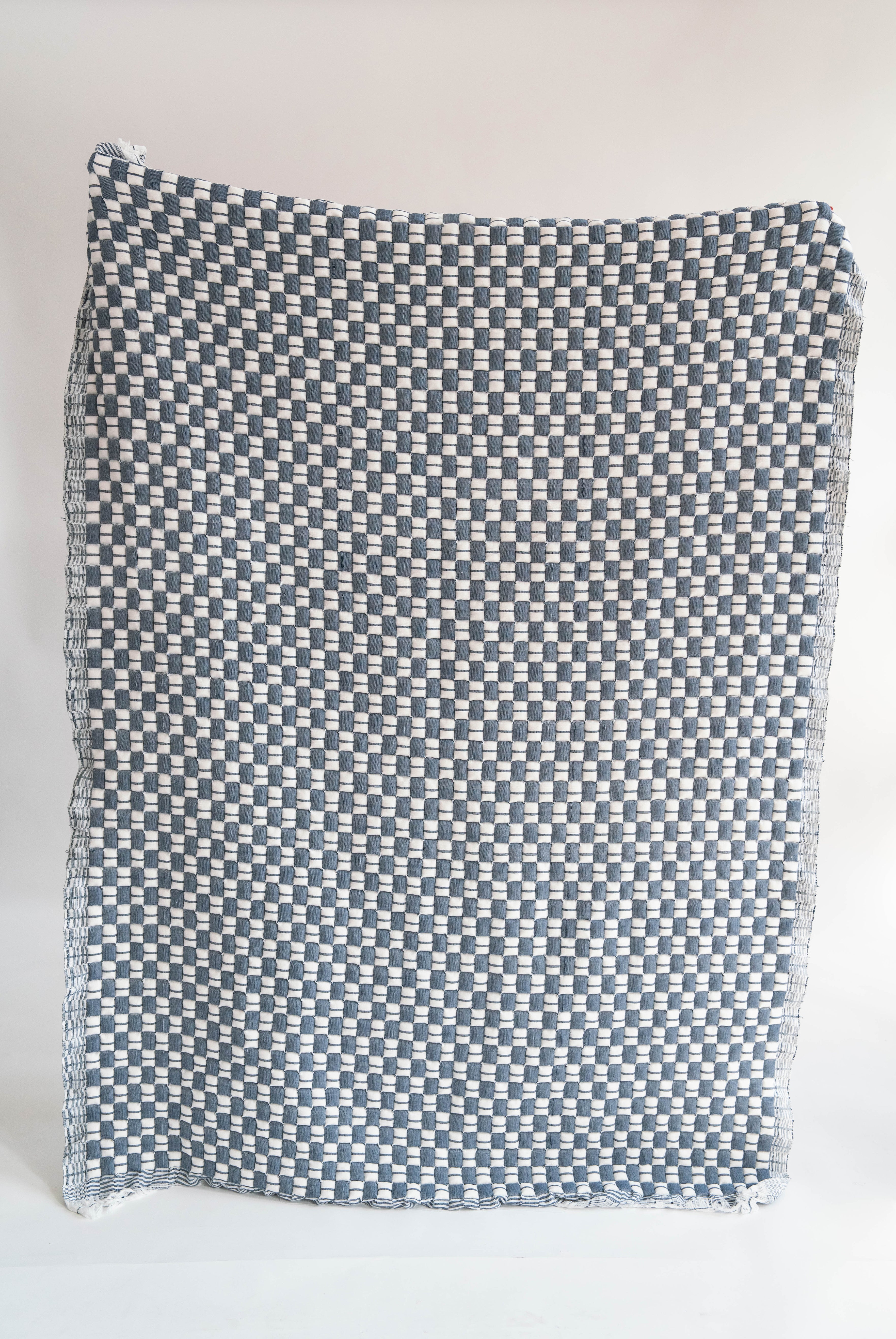 Blue checkered Sujani quilt with frayed edges, displayed flat