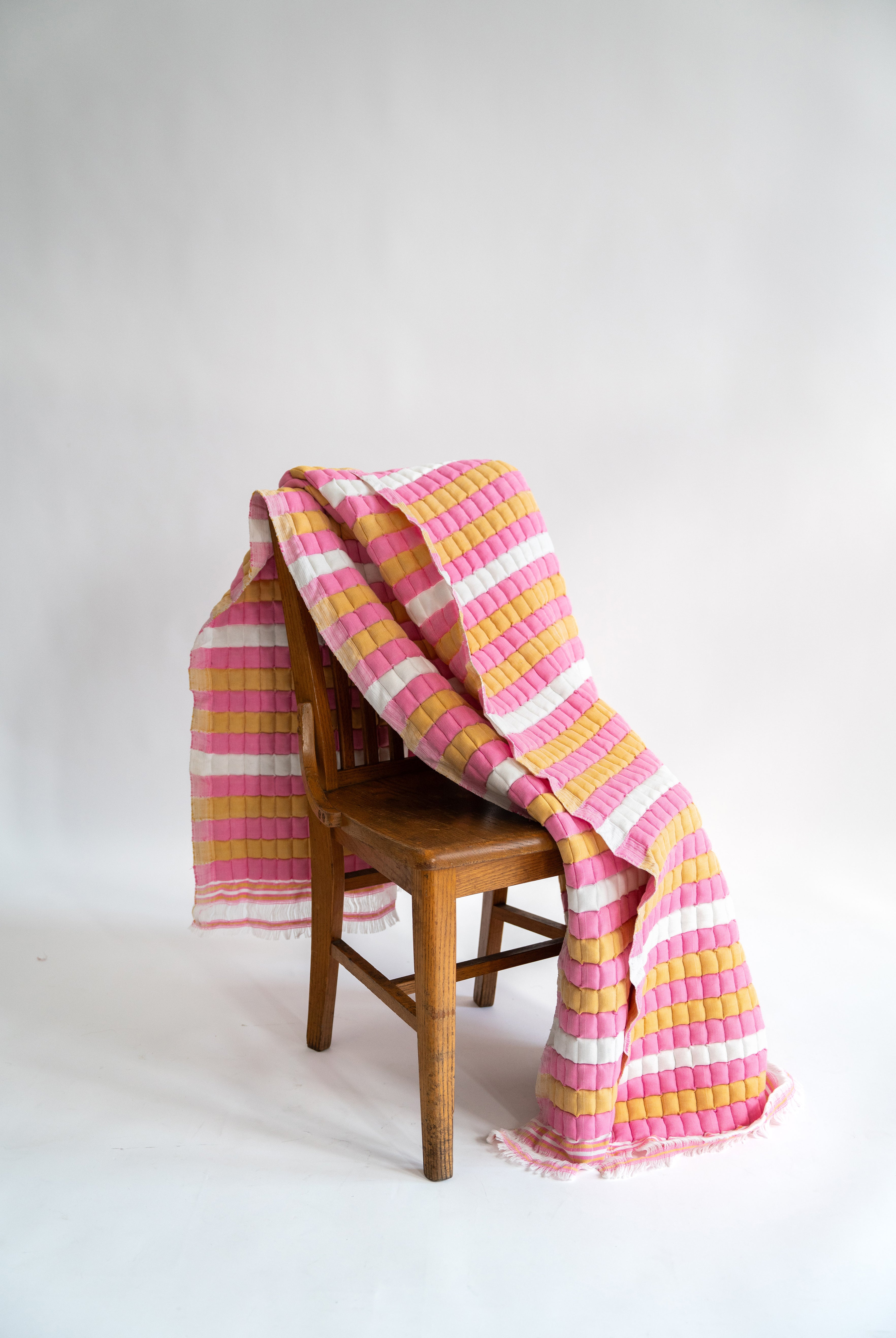 Pink and yellow striped Grand Budapest Sujani quilt draped over wooden chair - Inner Child