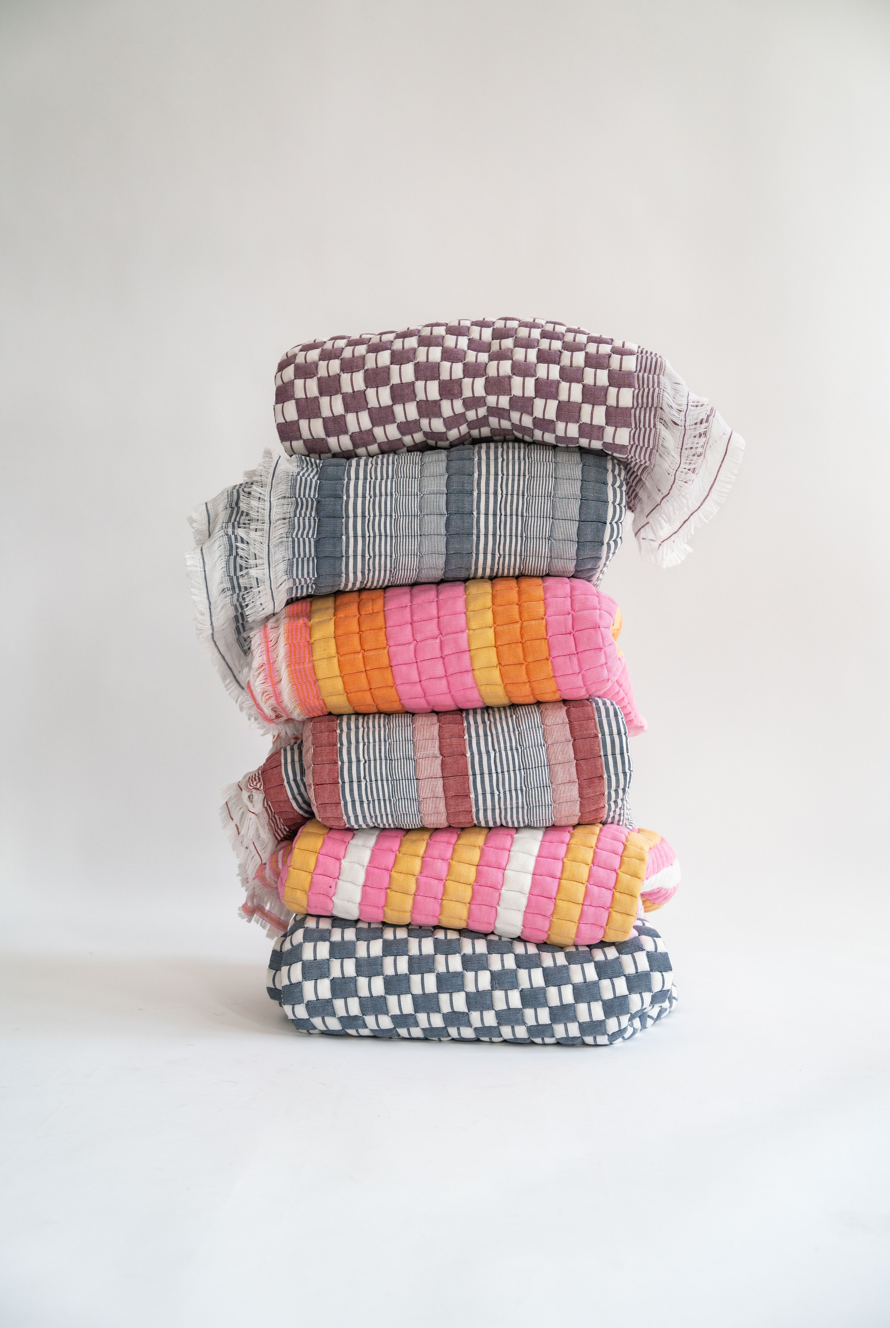 Colorful stacked Sujani quilts with checkered/striped patterns in pink/orange/gray hues