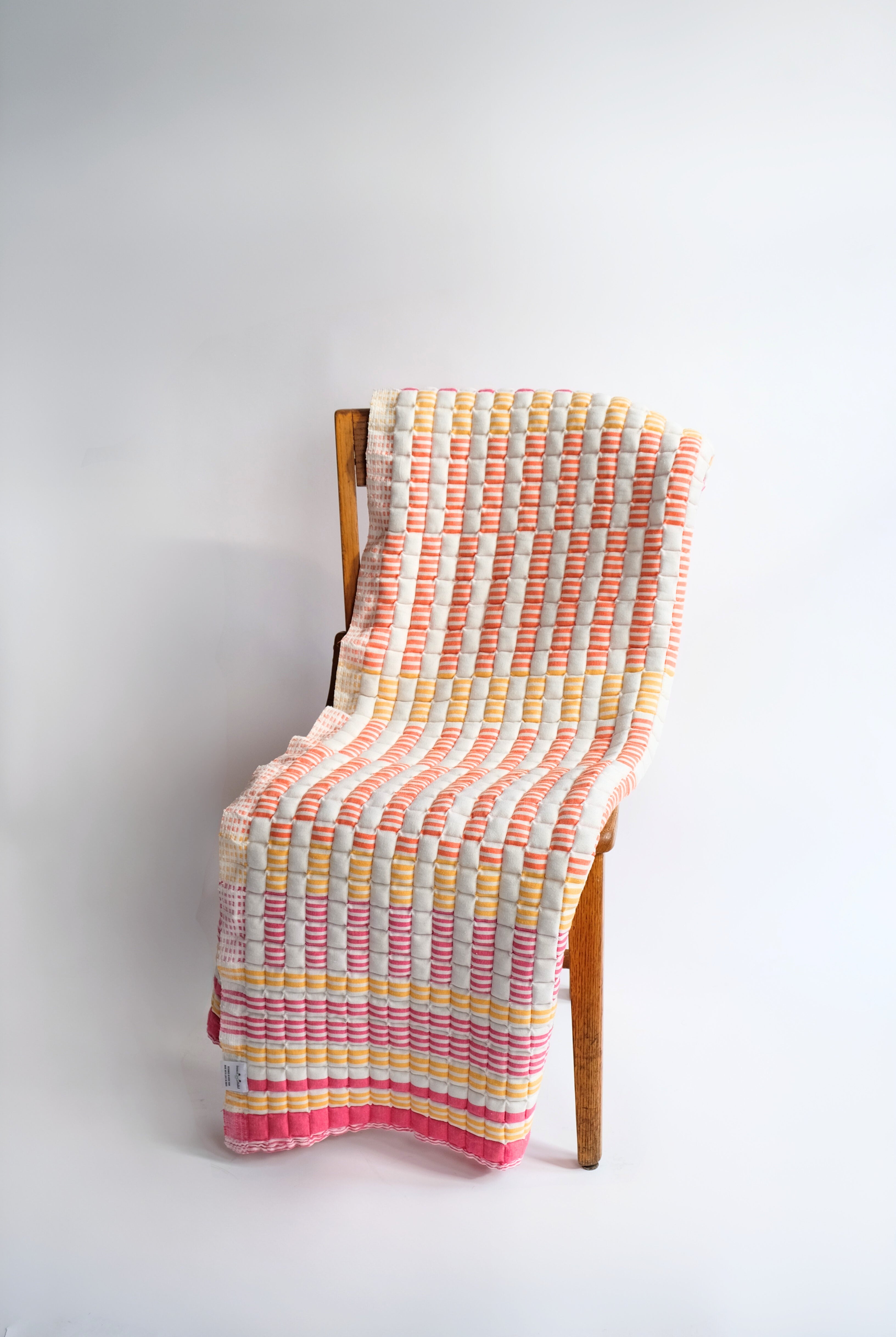 Inner Child sunset sujani quilt with pink, yellow, orange stripes draped on wooden chair