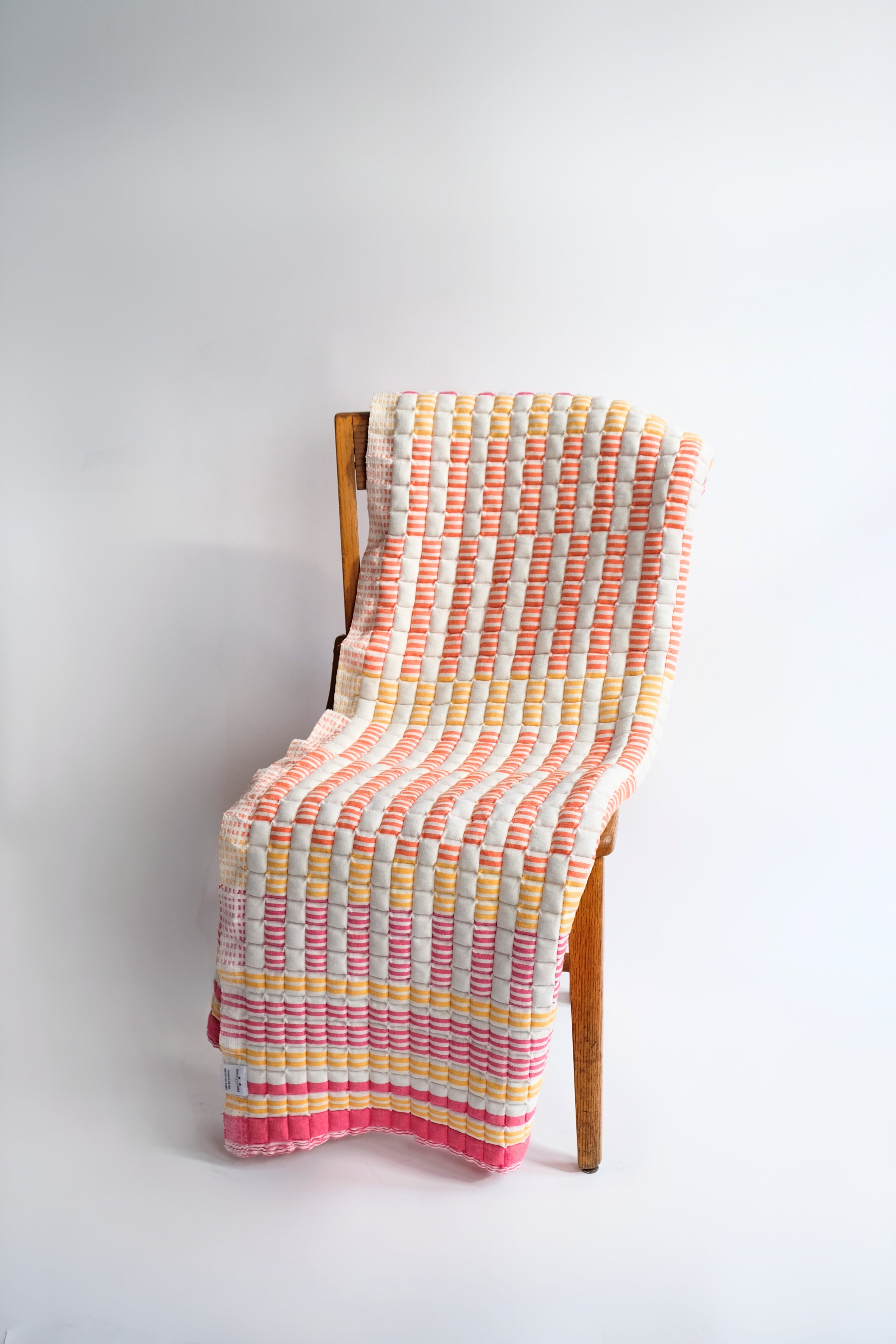 Inner Child sunset sujani quilt with pink, yellow, orange stripes draped on wooden chair