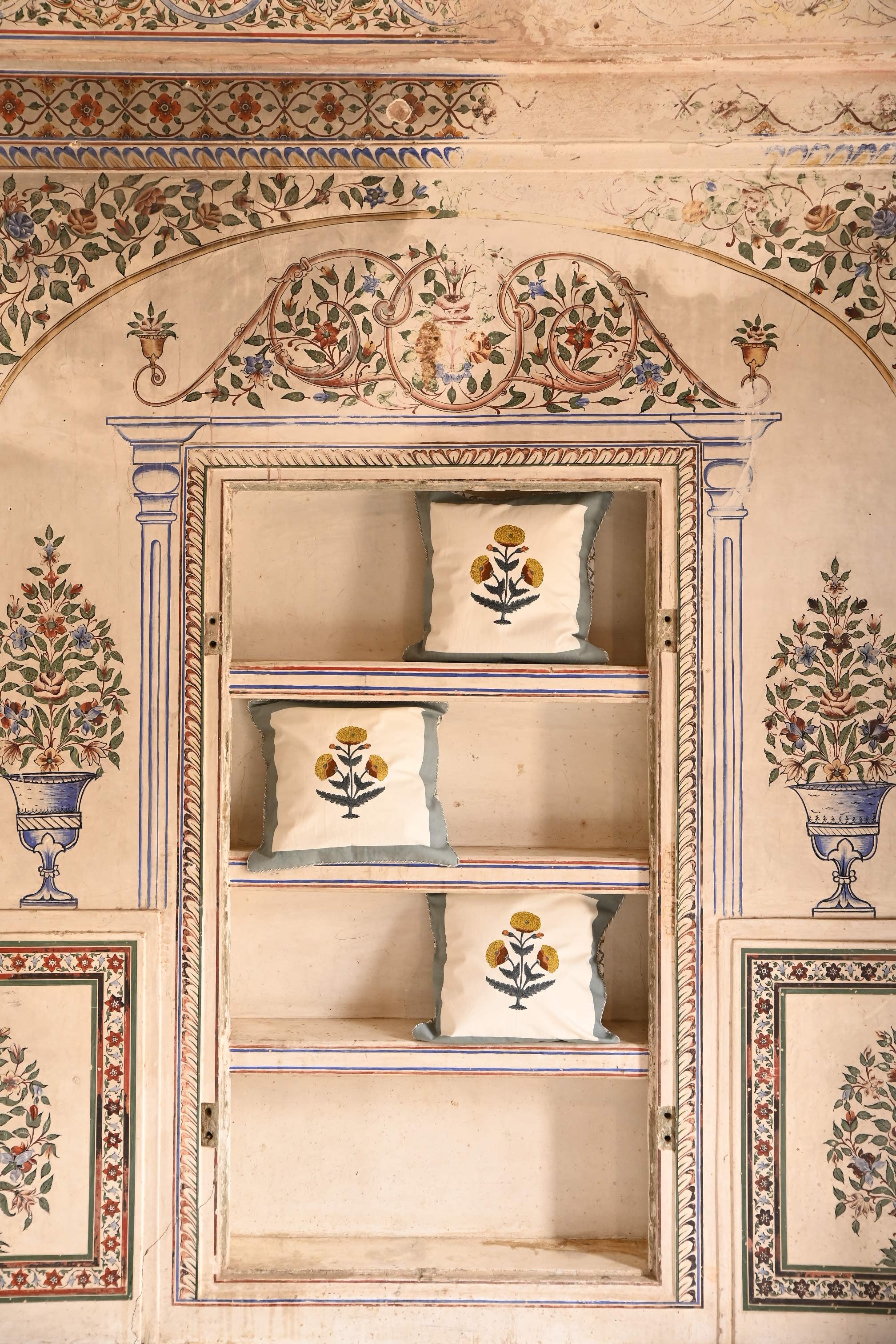 Three blue poppy blockprint pillows arranged on ornate wall shelf with painted floral decorations