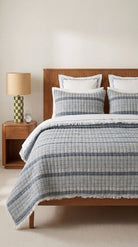 Bedroom with wooden bed, checkered blue and white duvet, and lamp on nightstand.