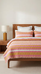 Bed with pink and yellow striped bedding in a bedroom setting.