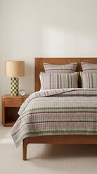 Bedroom with wooden bed, plaid bedding, and nightstand with lamp.