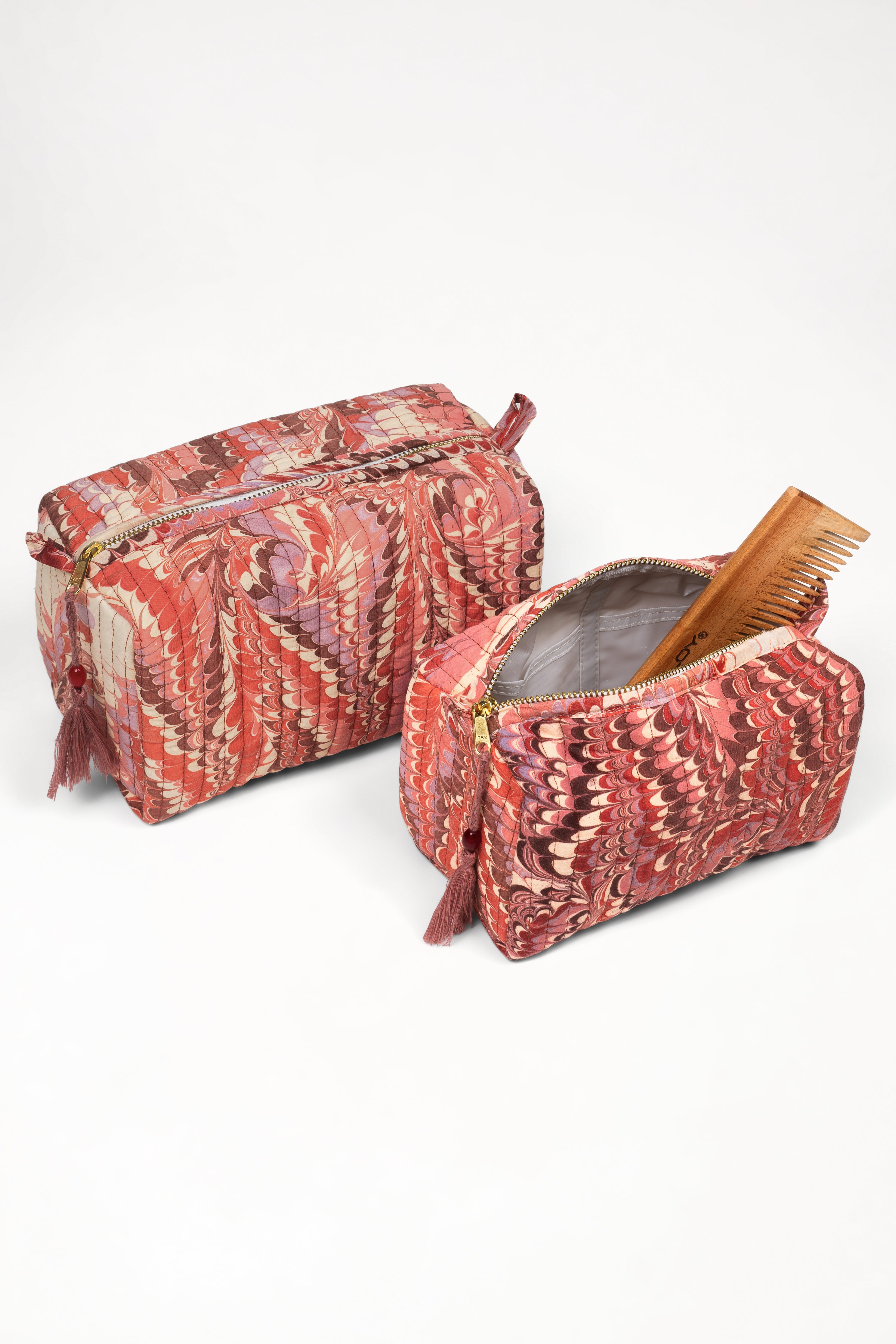 Two florentine pink hand-marbled quilted cosmetic bags, one open with wooden comb