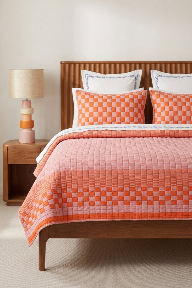 Bed with orange checkered quilt and wooden headboard in a room with a lamp.