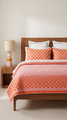 Bed with orange checkered quilt and wooden headboard in a room with a lamp.