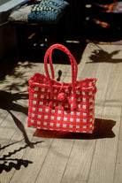 Bright red and white checkered recycled plastic Saigon Birkin bag with braided handles, displayed on wooden floor