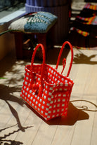 Bright red and white checkered recycled plastic Saigon Birkin bag with braided handles, positioned on wooden floor