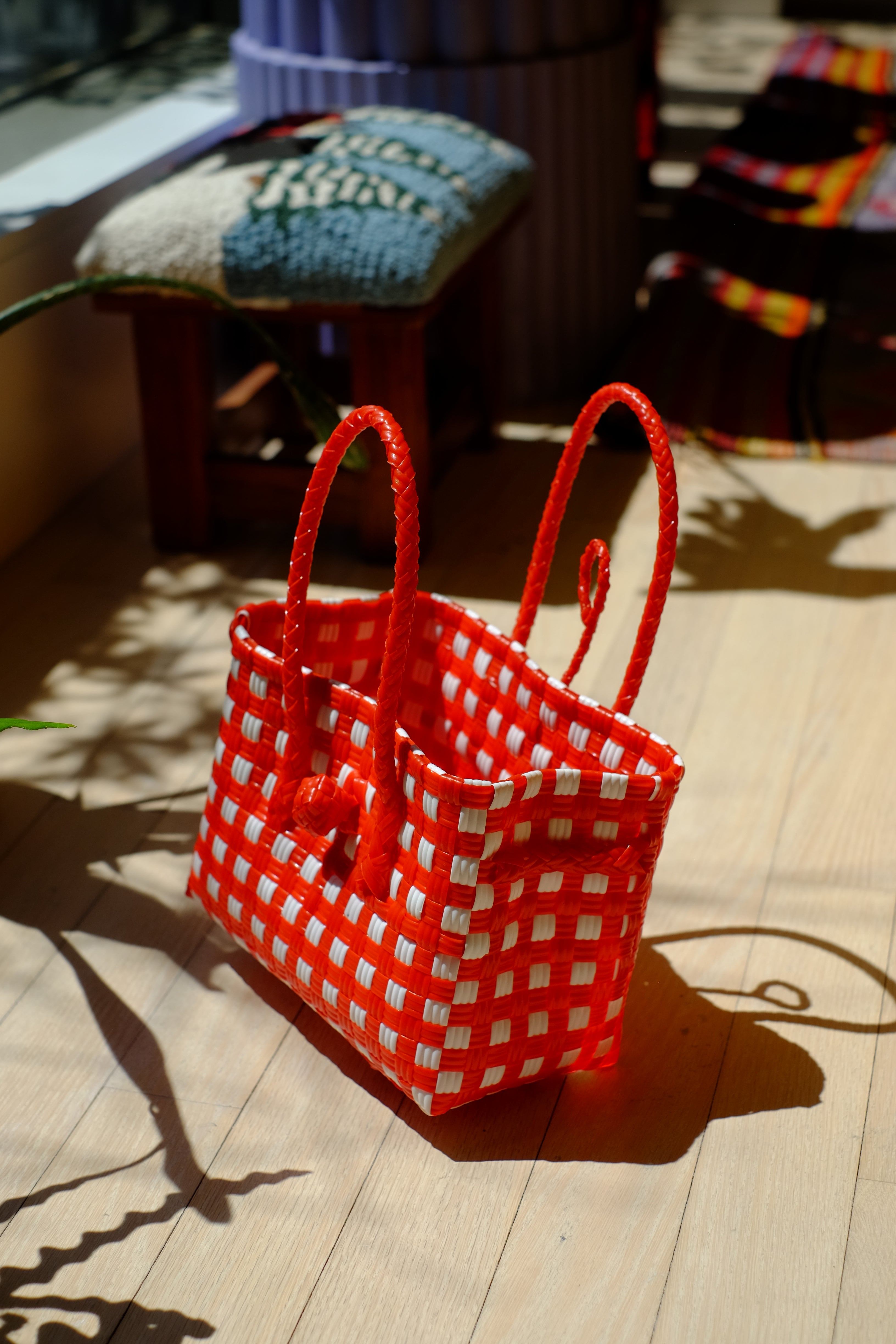 Bright red and white checkered recycled plastic Saigon Birkin bag with braided handles, positioned on wooden floor