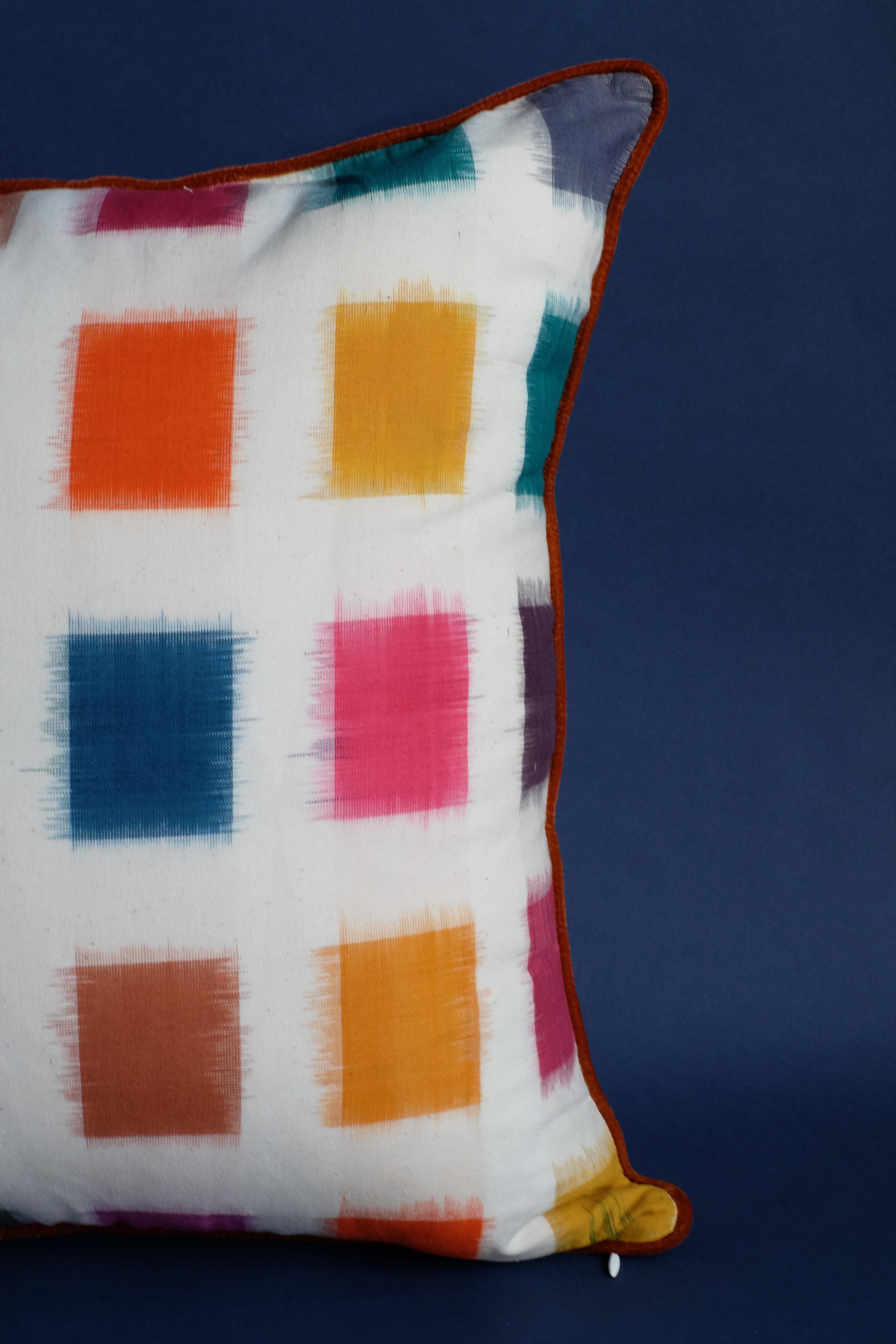 Close-up technicolor ikat pillow with brown trim - dark blue background