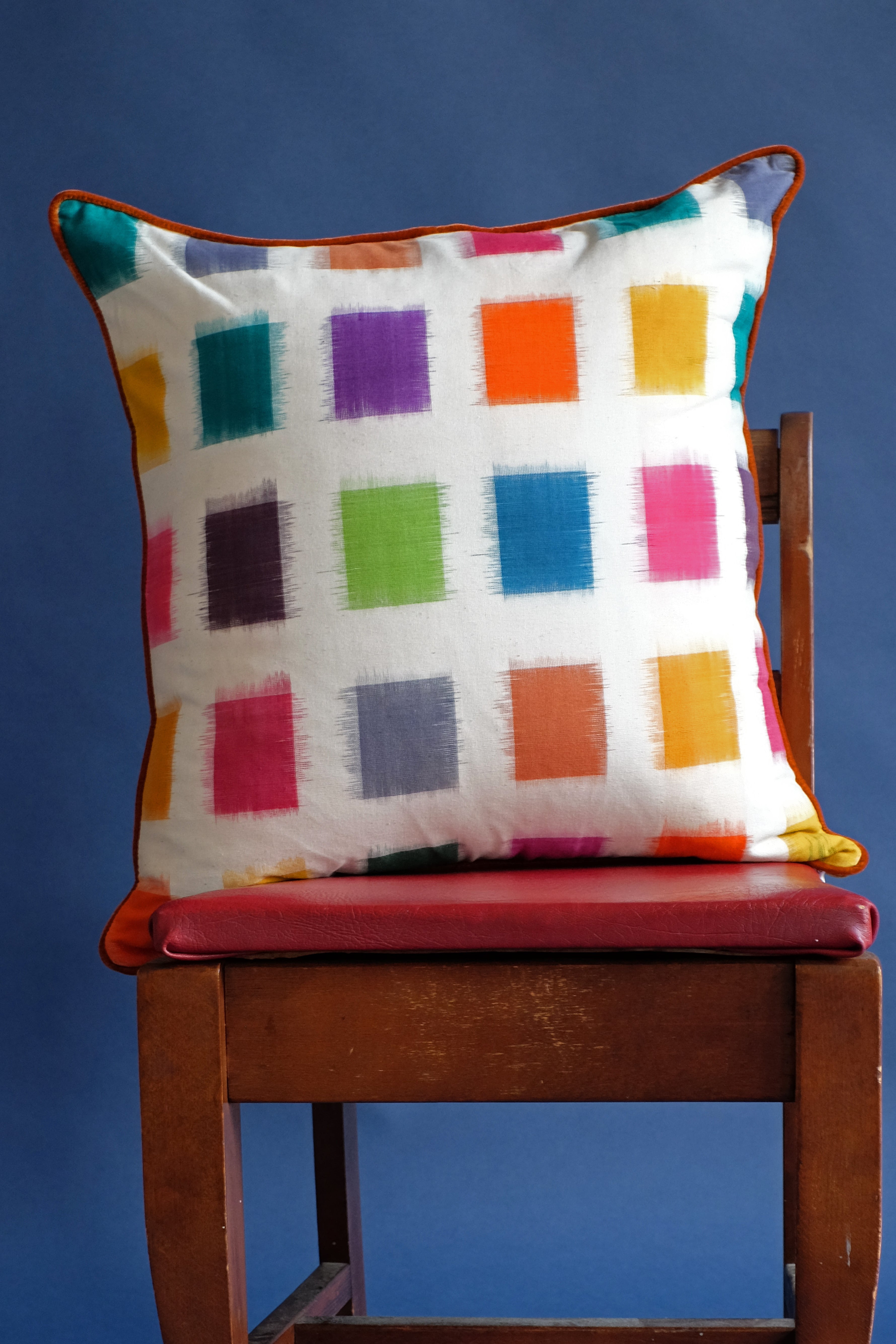 Technicolor ikat pillow with brown trim on wooden chair with red seat